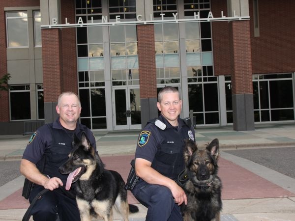 Officer Greg Rowe with Gunner and Officer Mark Allen with Remy in front of Blaine City Hall