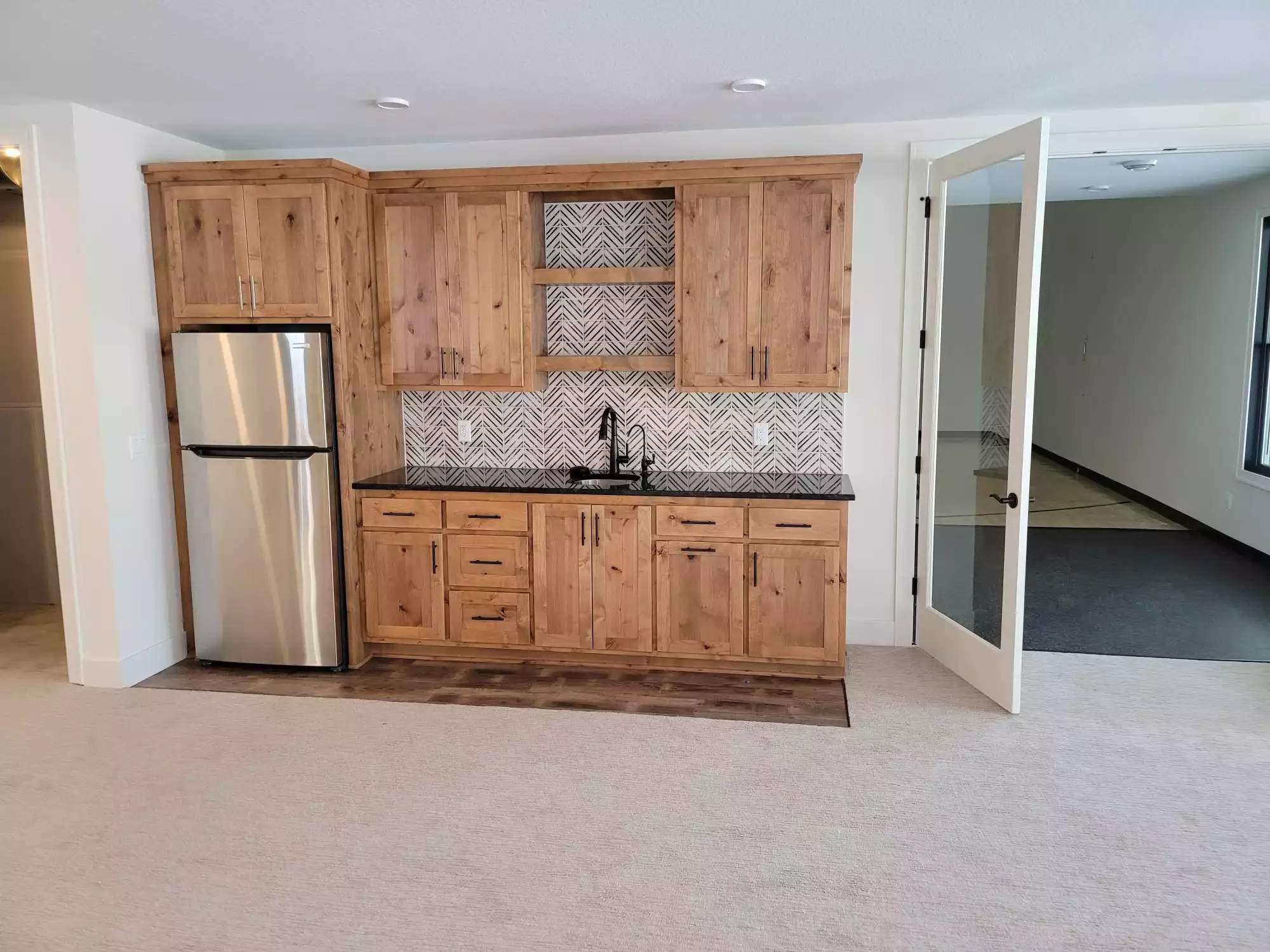 Wood stained cabinet wet bar with black solid counter and tile backsplash