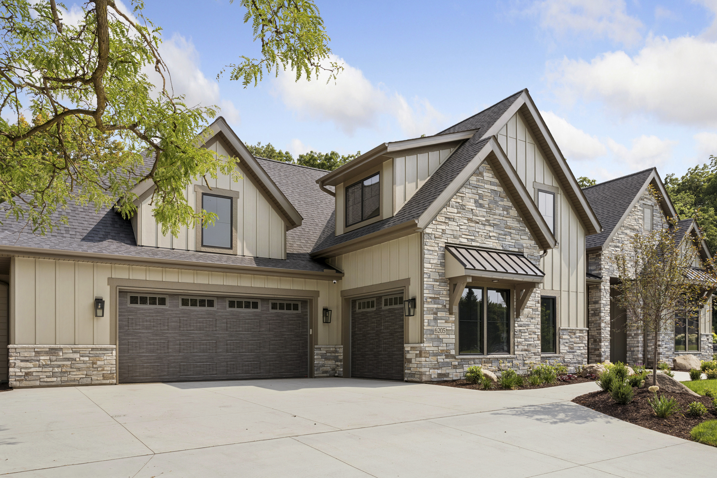 Three-car garage and front exterior of the 6205 Hillside home featuring stonework, board and batten siding, and metal roof accents.