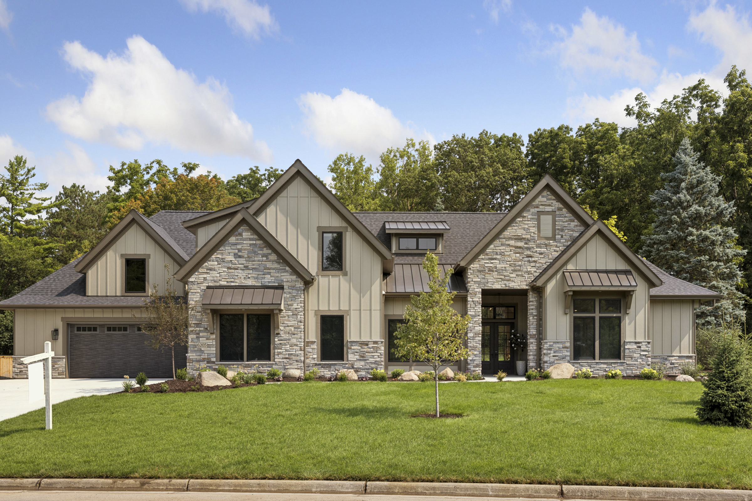 Full front view of the 6205 Hillside luxury home in Edina with stone exterior, board and batten siding, and expansive landscaped lawn.