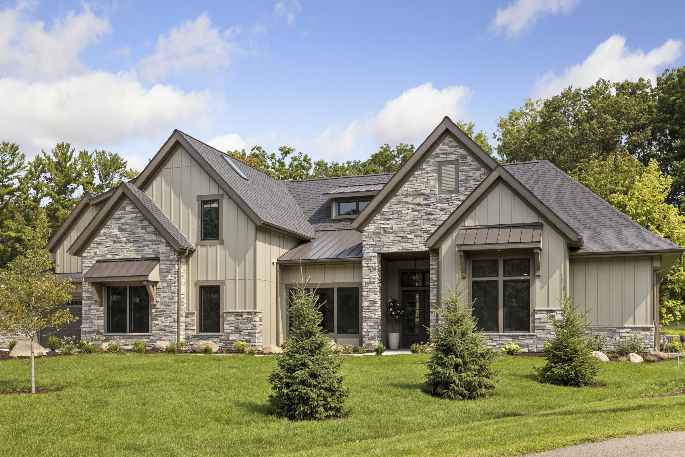 Front exterior of 6205 Hillside with stone and board and batten siding, covered entry, metal roof accents, and landscaped lawn.