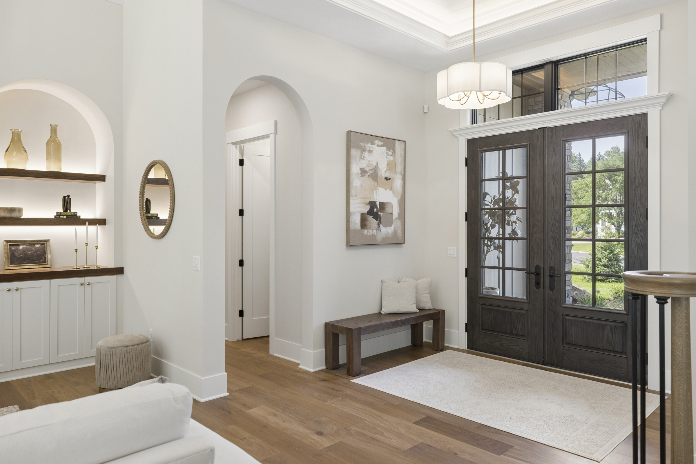 Bright entry foyer at 6205 Hillside with double glass front doors, arched openings, hardwood flooring, and illuminated built-in shelving.