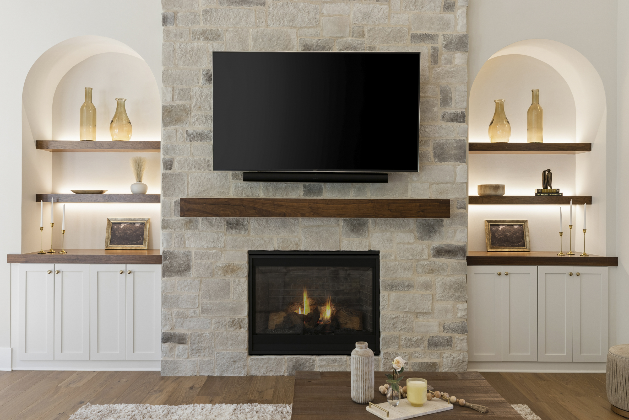 Great room fireplace at 6205 Hillside with floor-to-ceiling stone, wood mantel, built-in cabinetry, and illuminated arched display shelves.