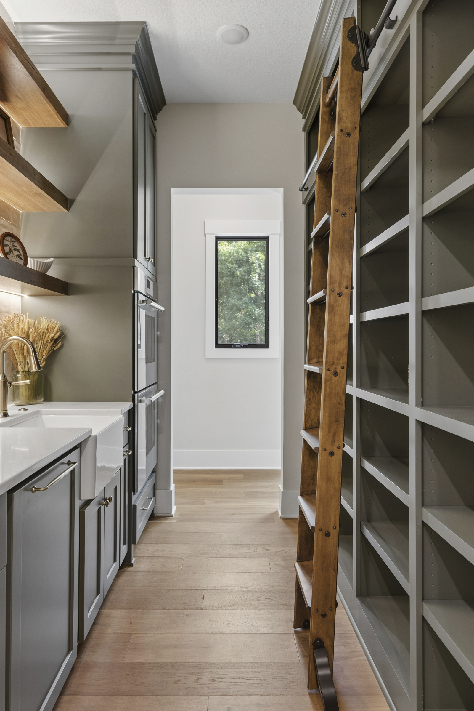 Butler's pantry at 6205 Hillside with custom dark cabinetry, farmhouse sink, built-in appliances, open wood shelving, and library ladder.