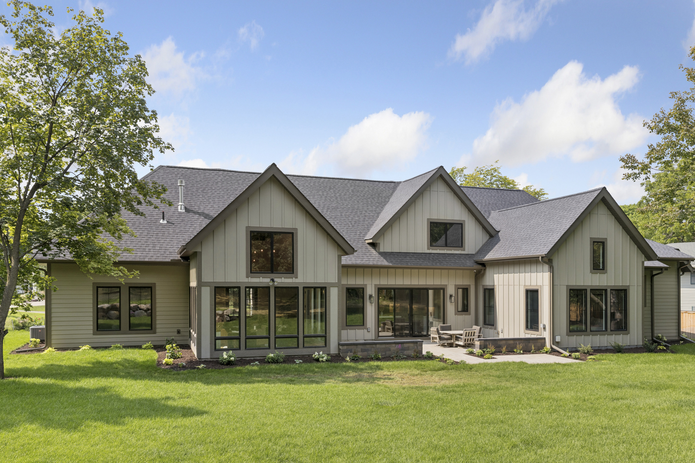 Rear exterior of the 6205 Hillside custom home with multiple gables, expansive black-framed windows, landscaped lawn, and outdoor patio.