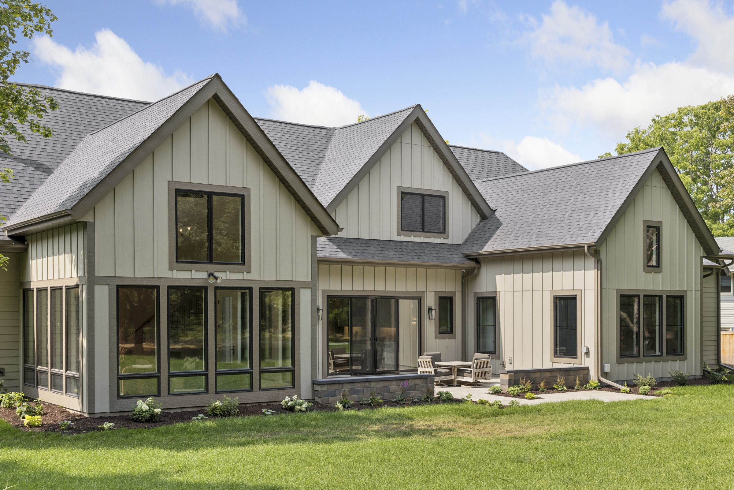Rear architectural detail of the 6205 Hillside home with board-and-batten siding, prominent gables, black-framed windows, and landscaped patio.