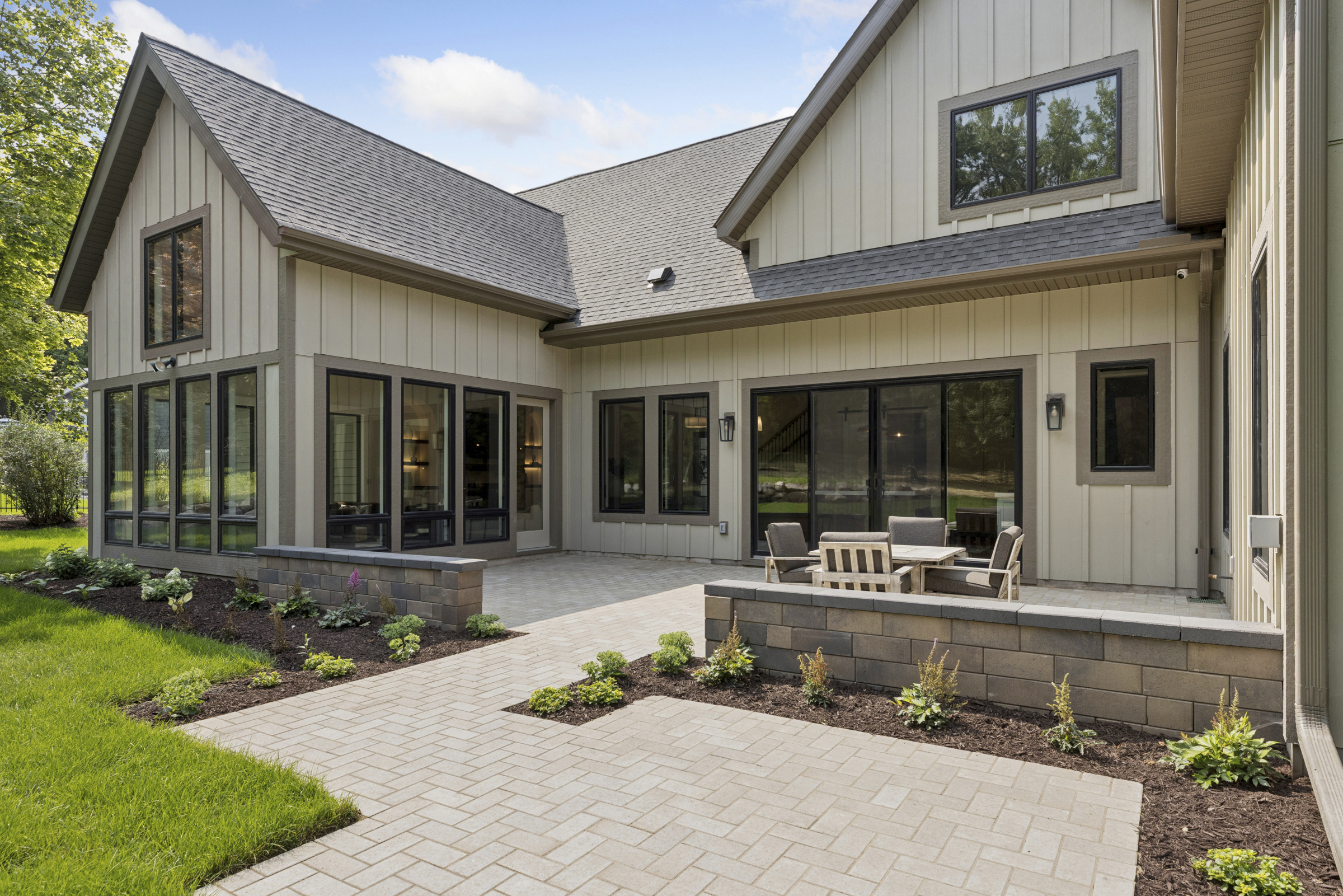 Outdoor living area at 6205 Hillside with paver patio, seating area, landscaped garden beds, and large black-framed windows overlooking the backyard.